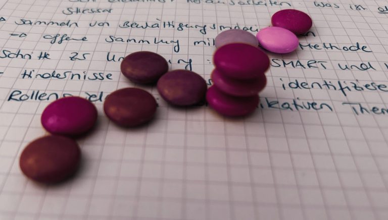 Schokolinsen Verschiedene lila und pinke Schokolinsen liegen auf kariertem Papier.