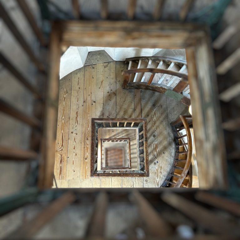 Holzspiraltreppe mit Blick von oben, schmaler Durchgang und in mehrere Ebenen unterteilt.