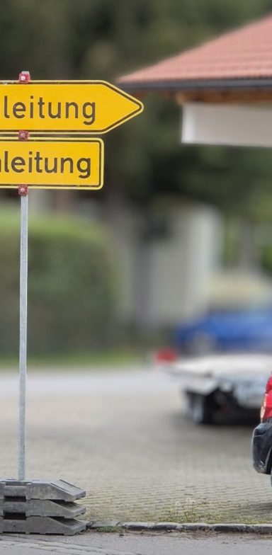 Umleitung Gelbe Wegweiser mit den Aufschriften "Richtung" und "Leitung" vor einem Gebäude.