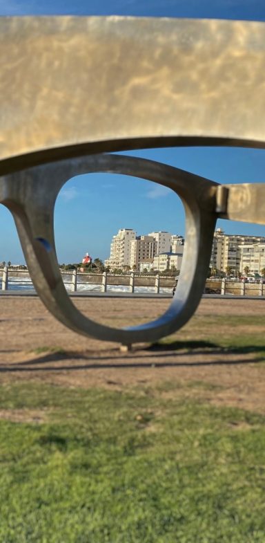 Brille Landschaft mit einer großen, geschwungenen Skulptur im Vordergrund und Stadtansicht im Hintergrund.